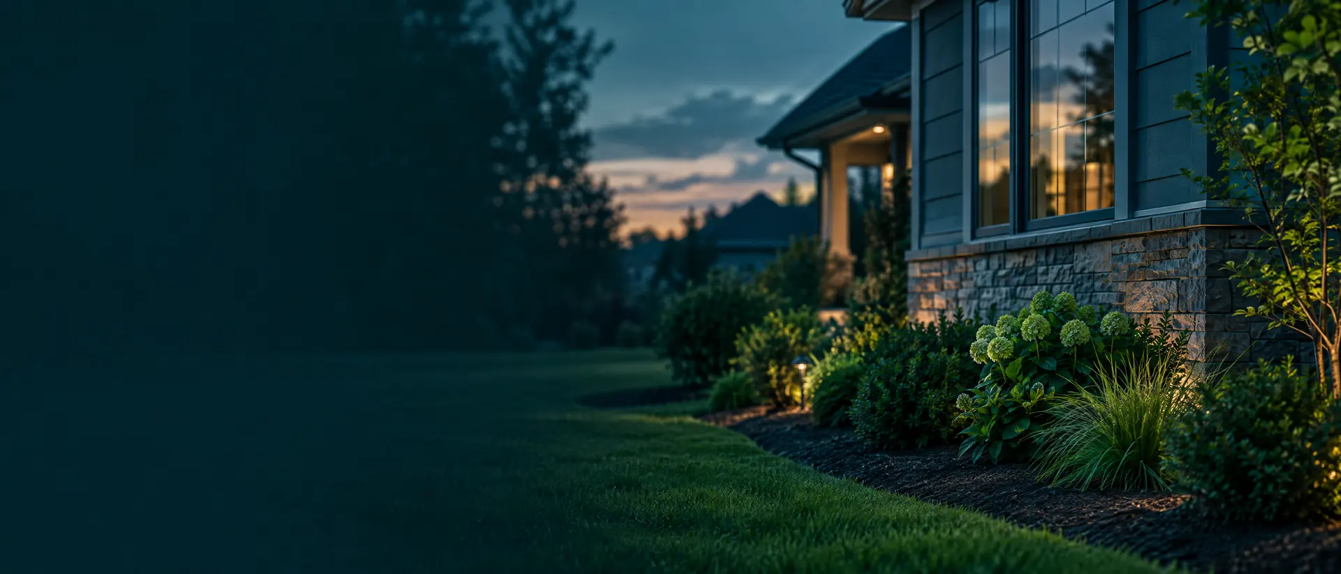Suburban house exterior at dusk with foundation bed and lawn edge
