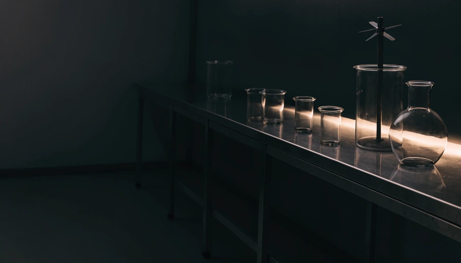 A stainless bench of glass beakers and a mixing vessel in a dim formulation laboratory.