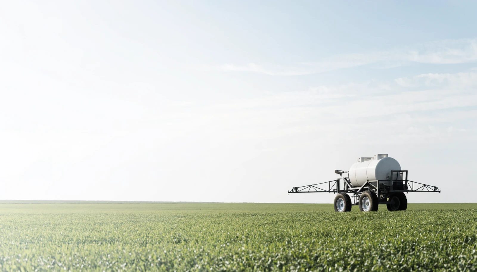 A boom sprayer at the edge of a green field under an open sky.